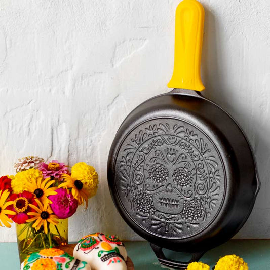 Decorative frying pan with skull design on a white wall with flowers and a cake.