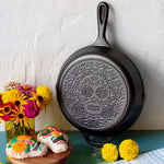 Black cast iron skillet with sugar skull design on a white surface with decorative items.