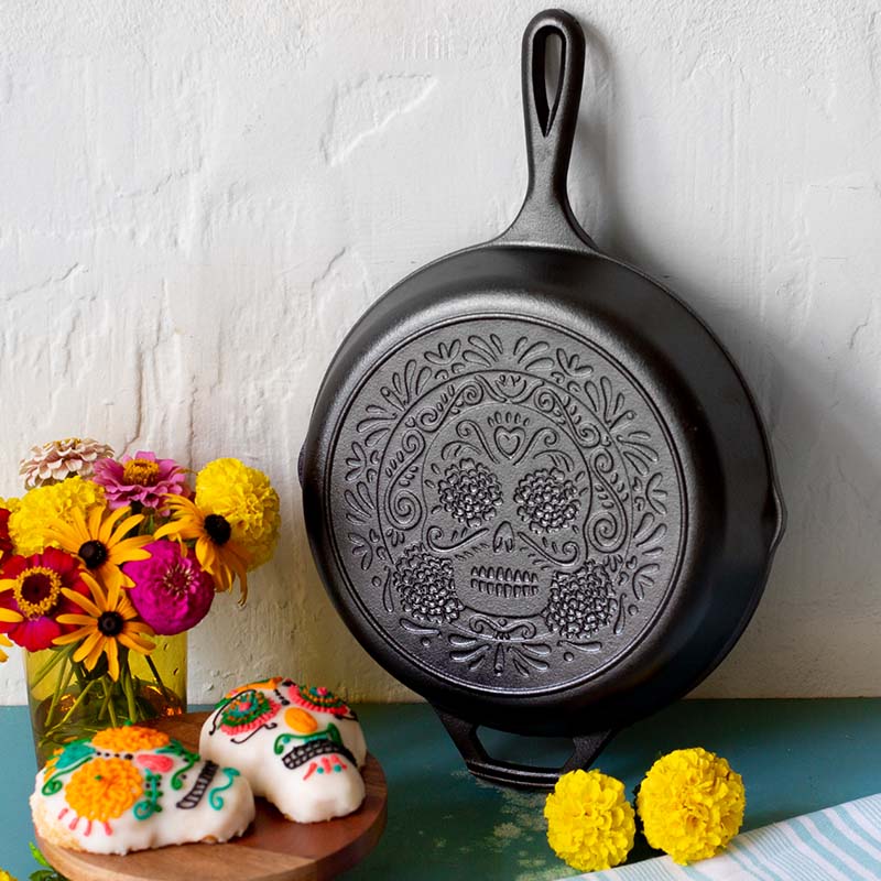 Black cast iron skillet with sugar skull design on a white surface with decorative items.