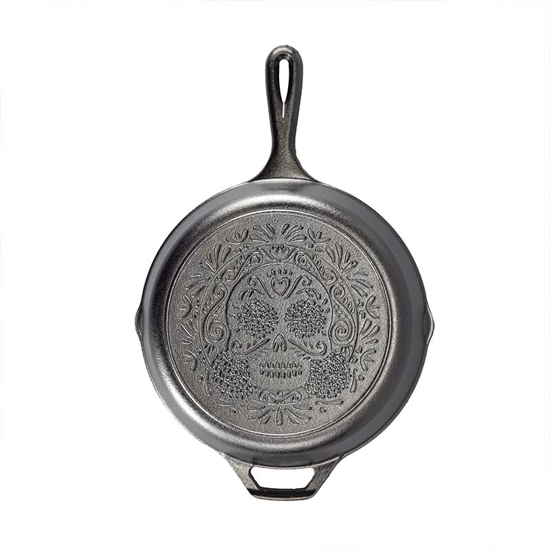 Black cast iron skillet with sugar skull design engraved on back.