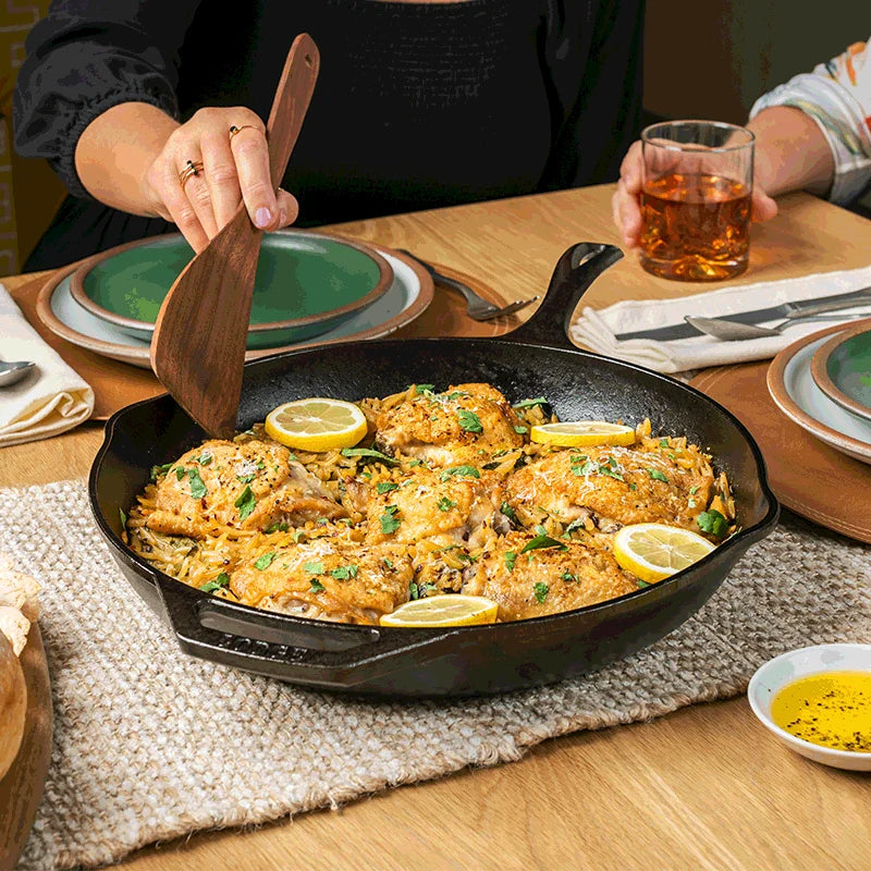 Chicken and lemon being served from skillet at table.