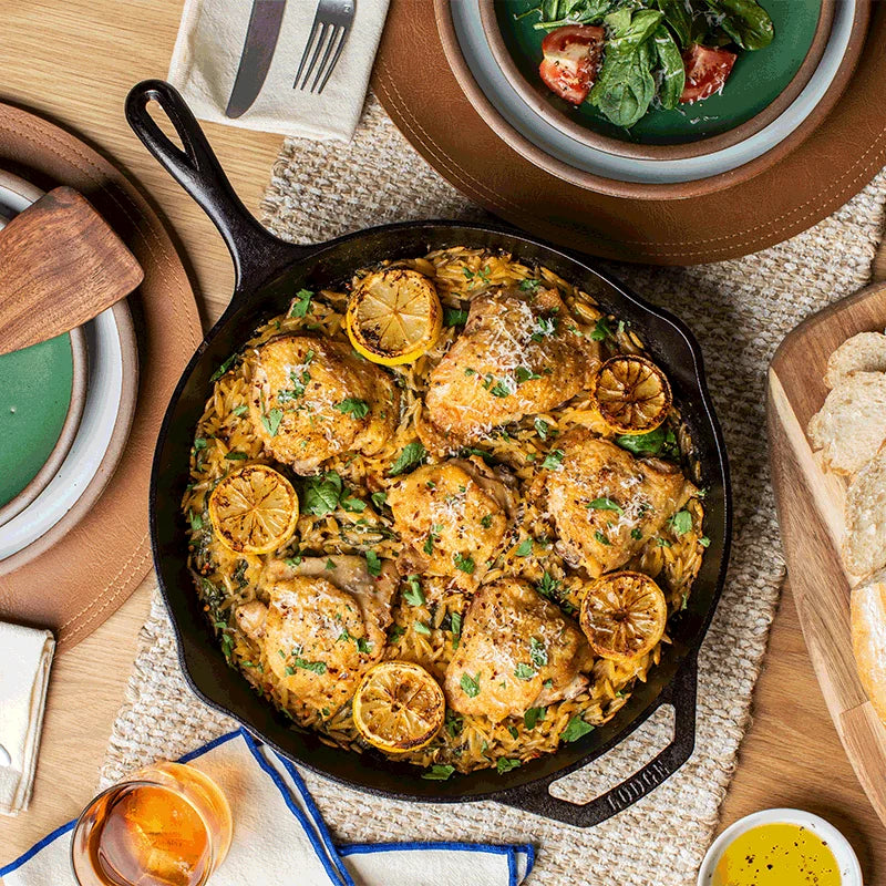 Chicken and lemon being served from skillet at table.