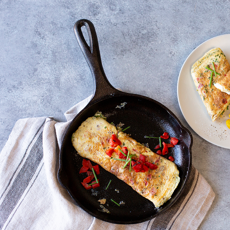 Fresh omelet topped with red peppers, served in skillet.
