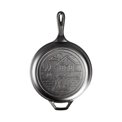 Skillet piece of combo cooker with a long handle, loop handles, and an engraved design of a cabin near a lake with a dog on the dock.