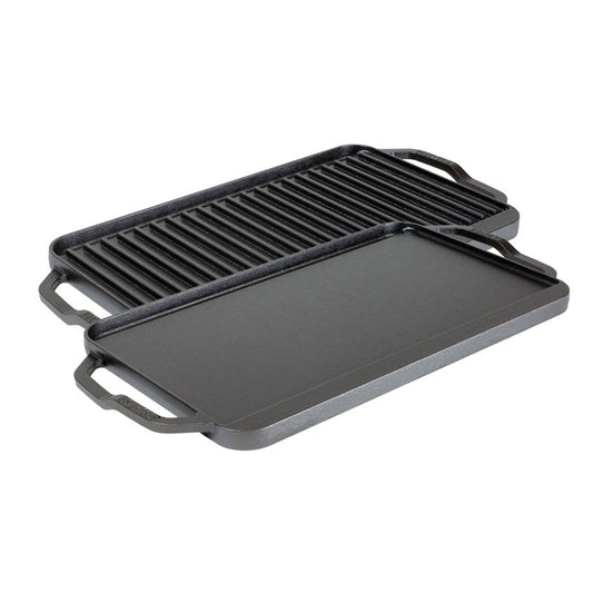 A reversible grill/griddle with one side featuring grooves for grilling and the other side flat, both sides Seasoned with a black seasoning, with lifted handles on the sides.