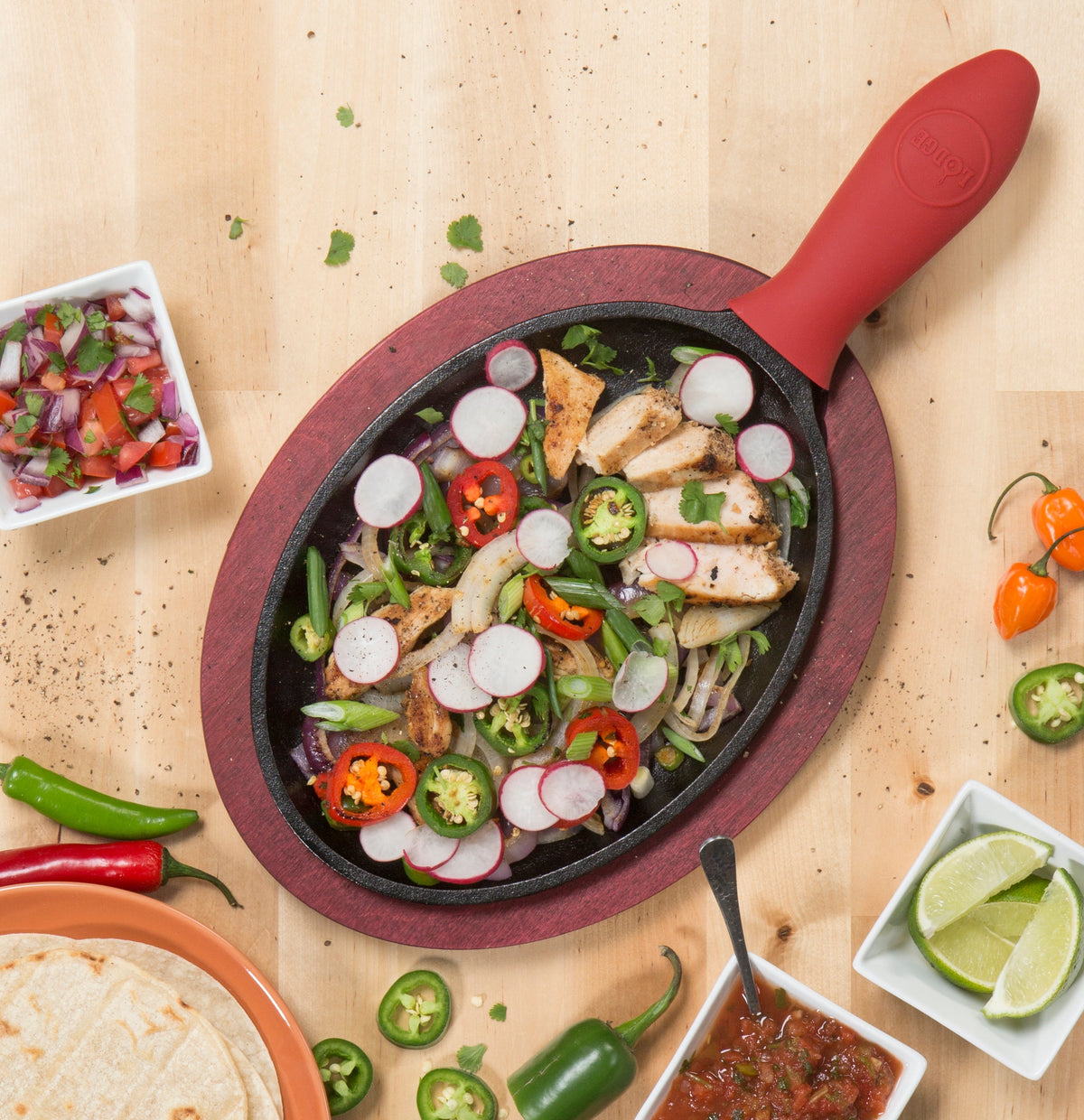 Freshly made chicken fajitas served on griddle in underliner near tortillas, limes, and slasa.