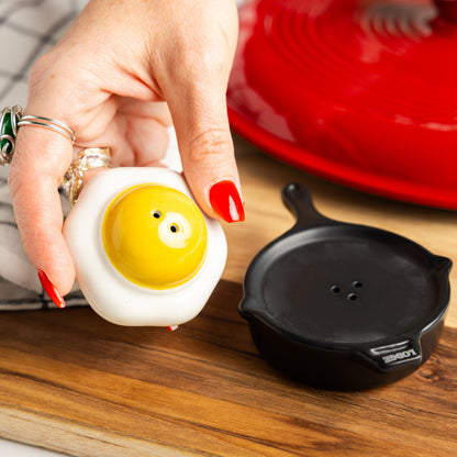 Person holding a small ceramic egg-shaped object with a yellow yolk on a wooden surface.