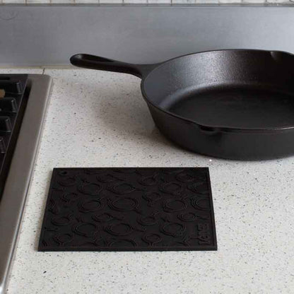 Black silicone trivet placed flat on counter next to stove and skillet.