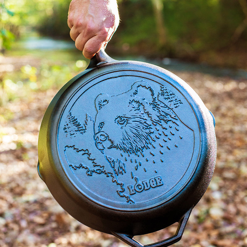 Someone holding skillet in a wooded area displayed embossed design on the back of skillet.