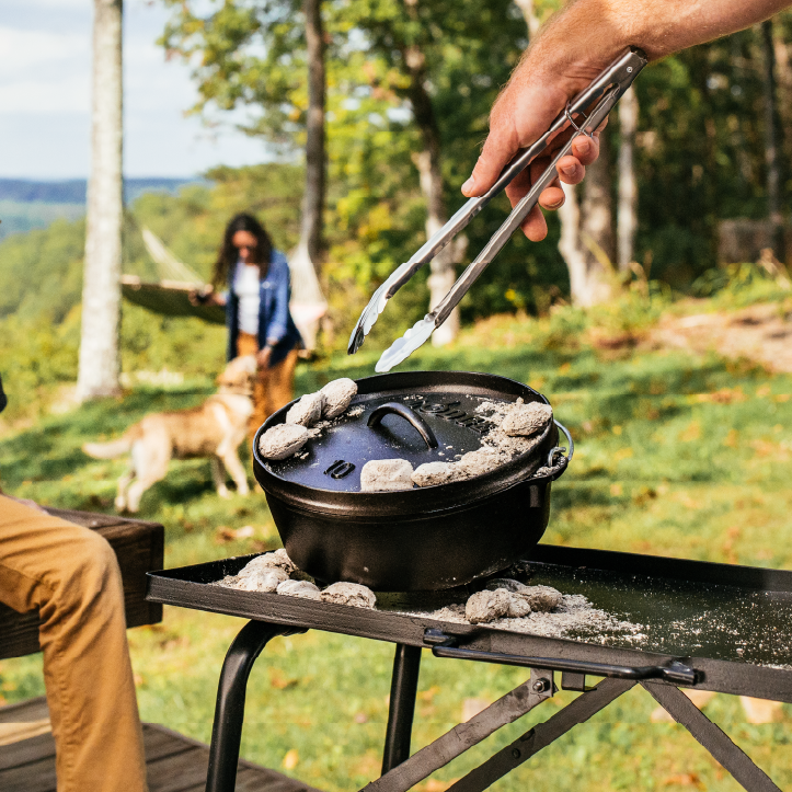 Someone moving coals on dutch oven lid while cooking.