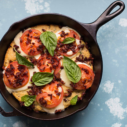 Freshly made meal garnished with tomatoes and basil in skillet.