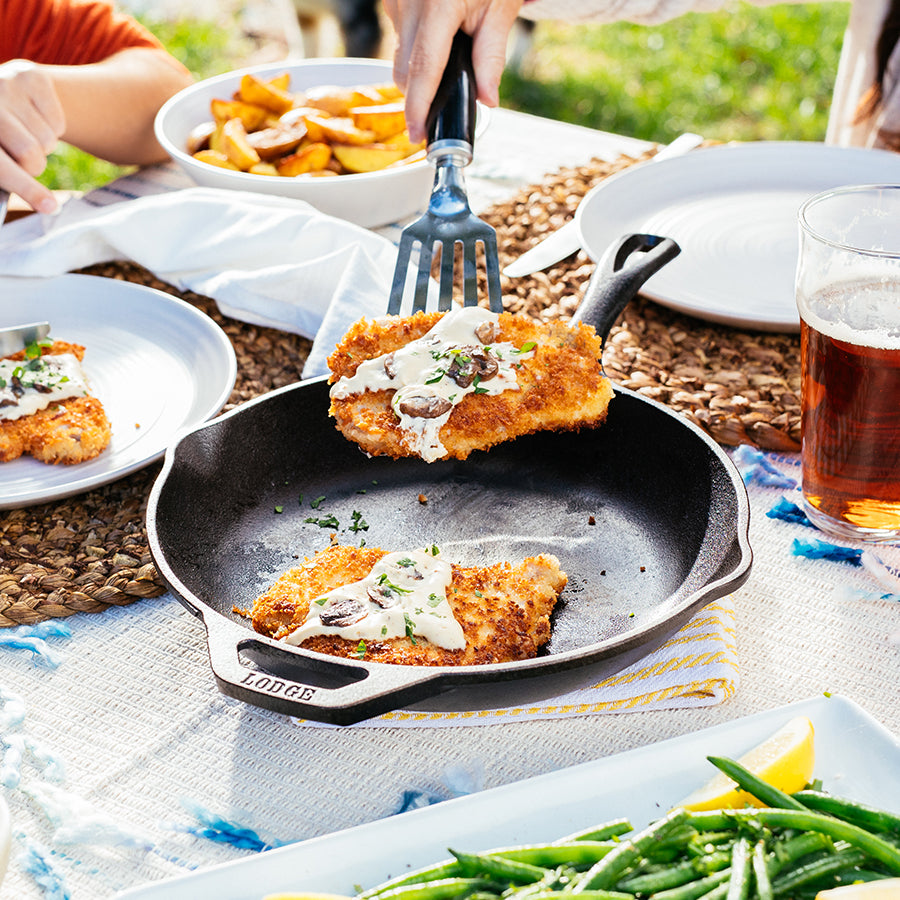 Schnitzel being served from skillet at table.