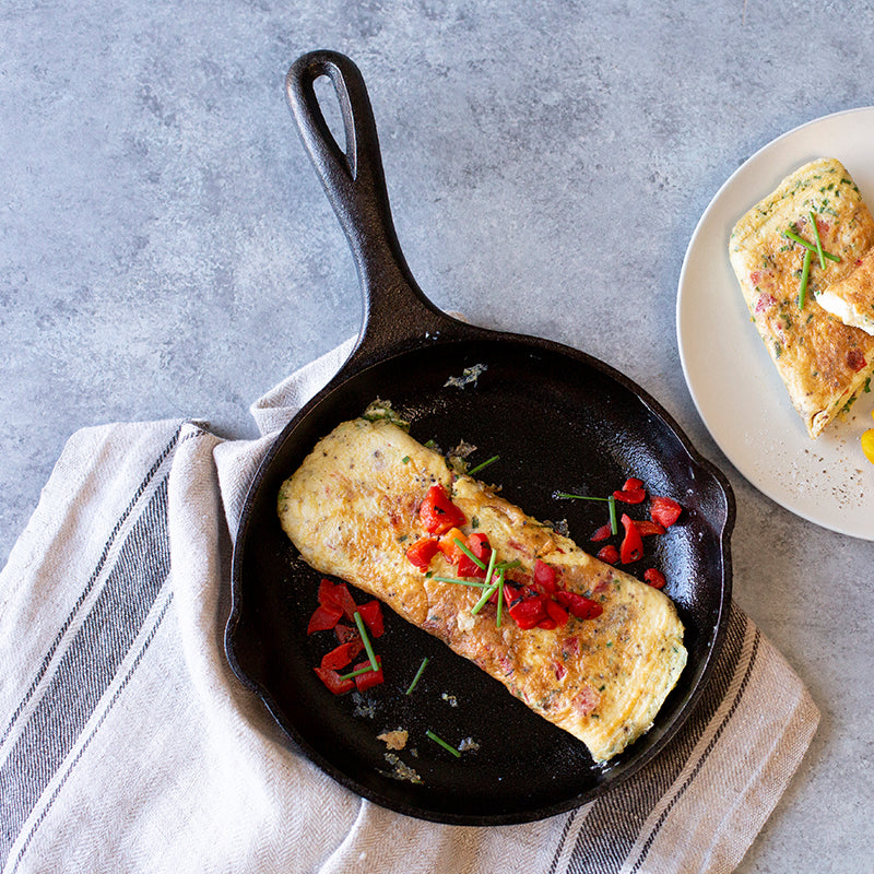 Fresh omelet topped with red peppers, served in skillet.