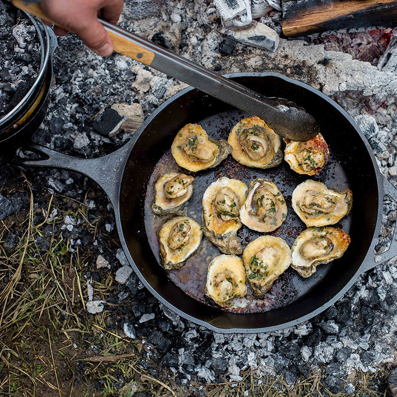 Someone turning mussels as they roast in skillet at campfire.