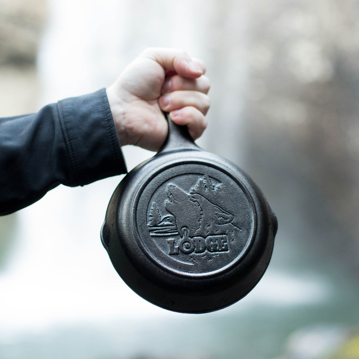 Someone holding skillet in front of waterfall displaying engraved design on the bottom.