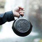 Someone holding skillet in front of waterfall displaying engraved design on the bottom.