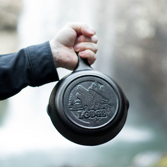 Someone holding skillet in front of waterfall displaying engraved design on the bottom.