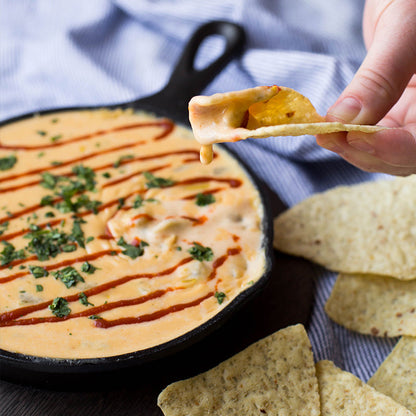 Someone using a chip to scoop queso prepared and served in skillet.
