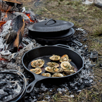 Oysters being cooked in skillet near campfire.